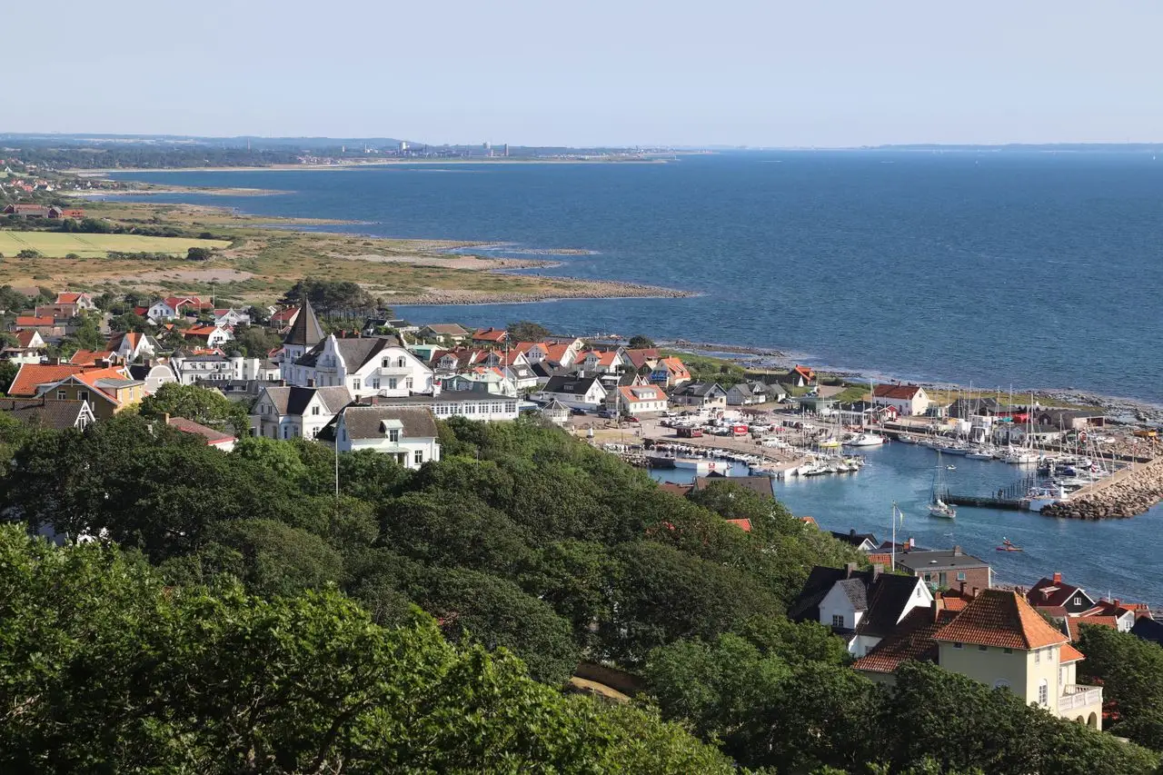 A picturesque view of Mölle's harbor and coastal town in Sweden with lush greenery and clear blue sea.