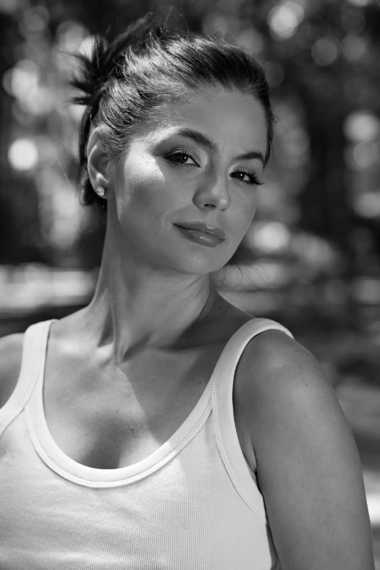 Black and white portrait of a confident woman in a white tank top against a soft focus background.